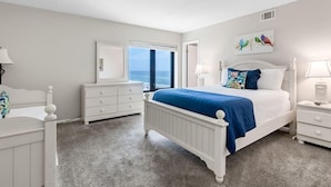 A bedroom with a white bed, white nightstands, a dresser, and a window with a view.