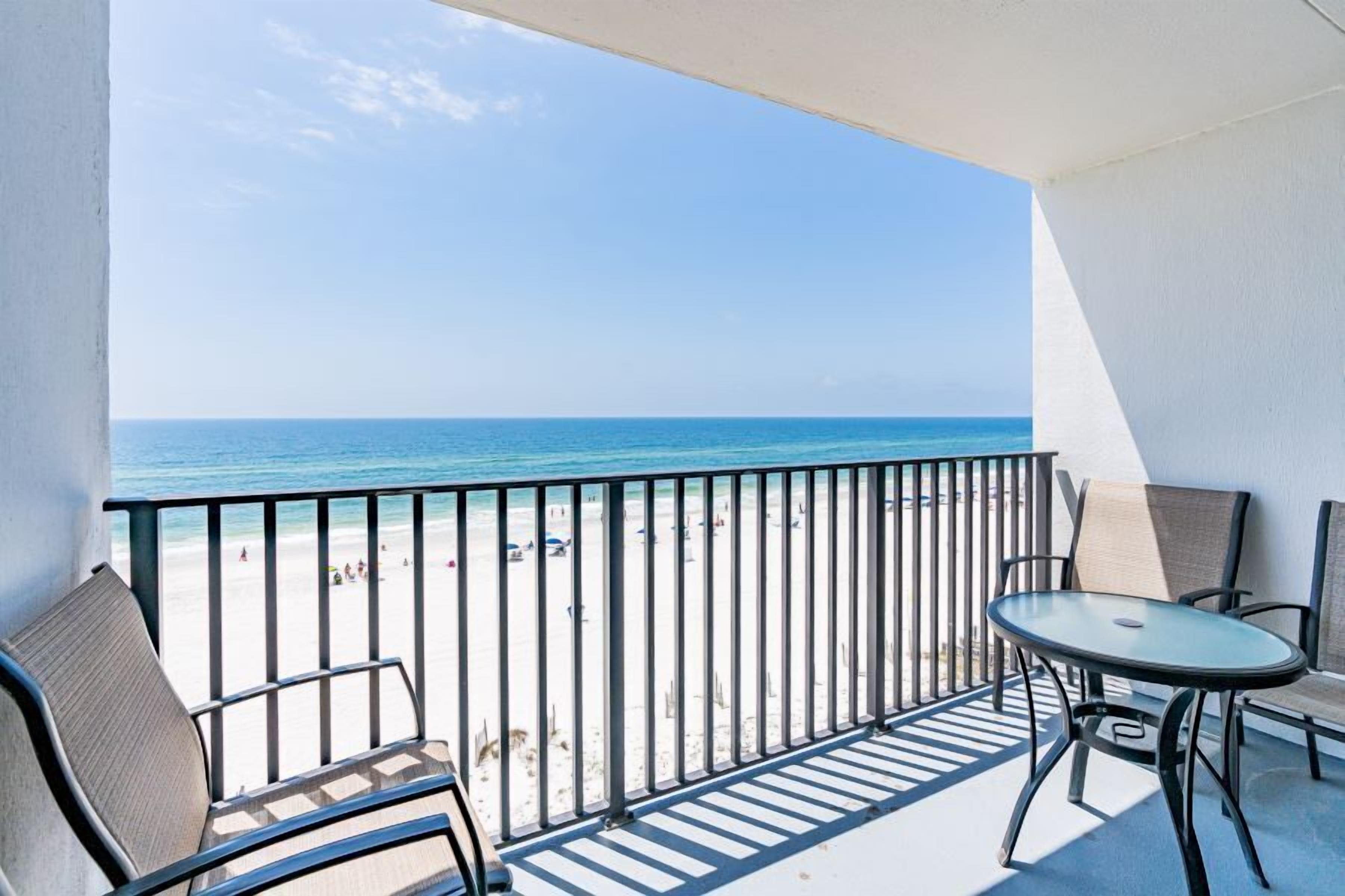 A balcony with a view of the beach, a table, and two chairs.