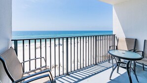 A balcony with a view of the beach, a table, and two chairs.