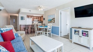 A living room with a sofa, a coffee table, a TV, and a kitchen area with a dining table and chairs.