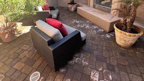 Une terrasse avec un canapé en osier, des plantes en pot et une cheminée.