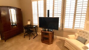Un salon avec un téléviseur posé sur un meuble, un canapé blanc, un buffet en bois et une table à manger avec des chaises.