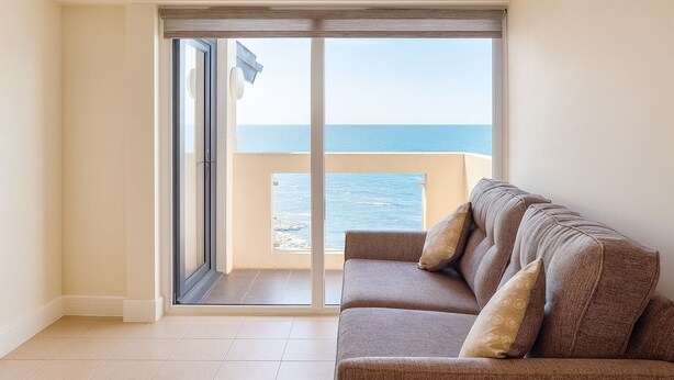 A balcony with a view of the sea, a sliding glass door, and a sofa with cushions. - Westbeach Holiday Apartments (Bideford)