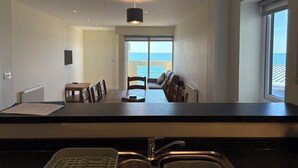 A modern kitchen with a sink, a dining area with chairs, and a view of the sea through a large window. - Westbeach Holiday Apartments (Bideford)