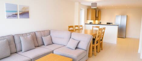 A modern living room with a grey sectional sofa, wooden coffee table, and a dining area with wooden chairs and a table.