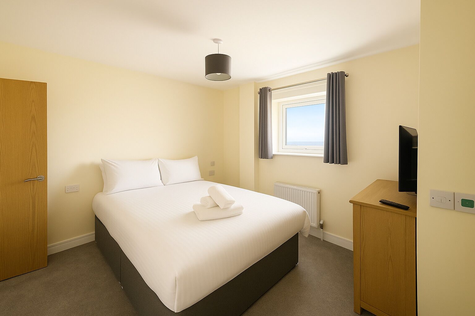 A neatly arranged hotel room with a single bed, a bedside table with a remote control, a television, and a window with curtains.