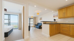 A modern apartment with a balcony, a kitchen with wooden cabinets, a dining area, and a living room with a sofa and a table. - Westbeach Holiday Apartments (Bideford)