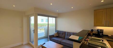 A compact living space with a kitchenette, a sofa, a coffee table, and a sliding glass door leading to a balcony.