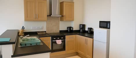 A compact kitchen with wooden cabinets, a stainless steel range, a microwave, and a coffee maker.