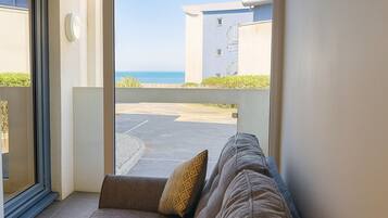 A view from a balcony with a sofa and cushions, overlooking a parking area and a building with a blue facade.