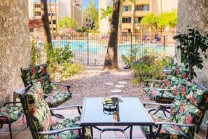 A poolside area with lounge chairs and a table, surrounded by a fence and trees. - Grnd Floor Pool View (Scottsdale)
