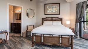 Une chambre avec un grand lit, un ventilateur de plafond, un tableau encadré, un miroir et une vue sur l’extérieur.