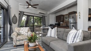 Un salon moderne avec un canapé gris, un fauteuil à motifs et une table basse en bois agrémentée d’une plante.
