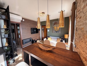 Una habitación de hotel moderna con una mesa de comedor de madera, una hamaca, un televisor y un cuadro de Buda.