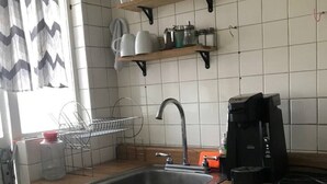 Une cuisine équipée d’un évier, d’une cuisinière et d’étagères au-dessus du plan de travail, où sont rangés divers ustensiles de cuisine.