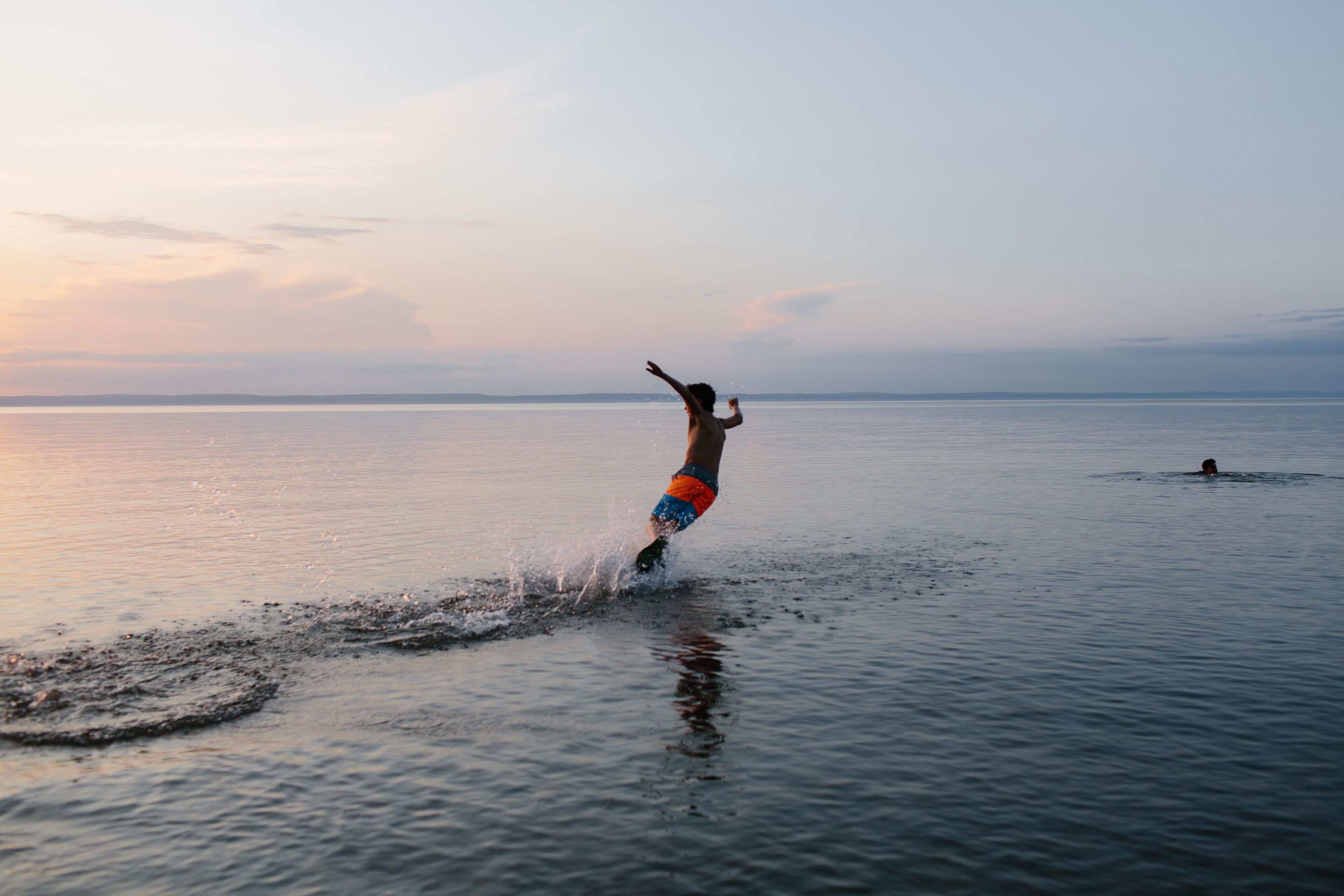 Eine Person fährt einen Wakeboard auf ruhigem Wasser bei Sonnenuntergang.