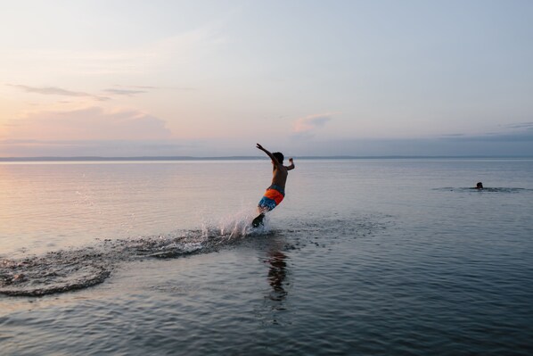 Eine Person fährt einen Wakeboard auf ruhigem Wasser bei Sonnenuntergang.