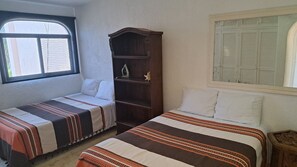 Une chambre avec deux lits, chacun doté de draps à rayures, une armoire en bois et une fenêtre avec des volets.