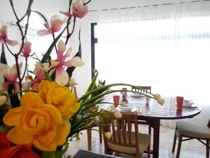 Un coin repas avec une table ronde, des chaises et un vase de fleurs.