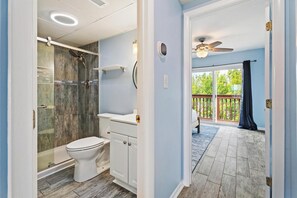 A bathroom with a shower, toilet, and sink, leading to a balcony with a view of trees. - Breezy Point #303 - Rooftop Deck Panoramic Sunsets (Ocean City)