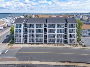 A multi-story building with large windows and balconies, located near a waterfront with a bridge in the background. - Breezy Point #303 - Rooftop Deck Panoramic Sunsets (Ocean City)