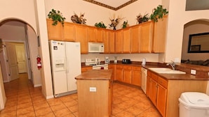 A kitchen with wooden cabinets, a refrigerator, a microwave, a sink, and a trash can. - 213 BS (Davenport)