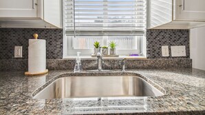 Una cocina con encimera de granito, pileta de acero inoxidable y muebles altos blancos.