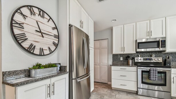 Una cocina moderna con armarios blancos, electrodomésticos de acero inoxidable, un reloj de pared grande y una encimera de granito.