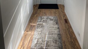 Ein Flur mit Holzboden, einer schwarzen Fußmatte, einer weißen Tür mit Fensterglas und drei abstrakten Wandbildern.