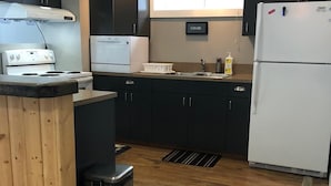 Eine moderne Küche mit dunklen Schränken, einer Edelstahl-Mülltonne, einem weißen Kühlschrank und einem eingebauten Backofen.