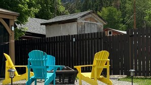 Eine Terrasse mit Adirondack-Stühlen in Blau und Gelb, einem kleinen Tisch und einem Holzzaun.