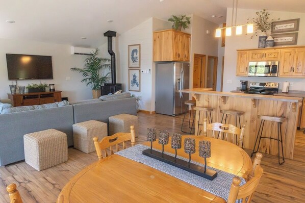 A modern living room with a sofa, ottomans, a dining table, and a kitchen area with wooden cabinets and a bar stool.