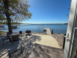 A deck with outdoor furniture overlooking a lake, a dock extending into the water, and a clear sky.