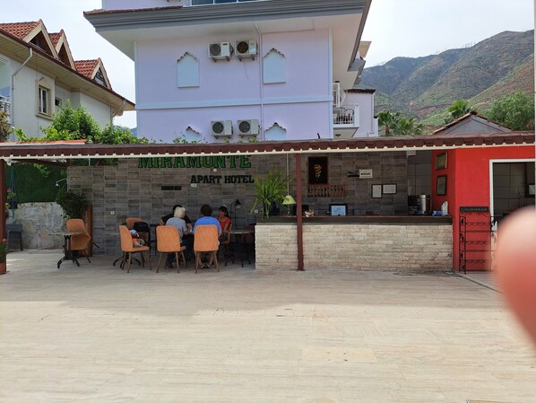 Zona d'estar exterior d'un hotel amb façana de pedra, unitats de aire condicionat i vistes del paisatge circumdant.