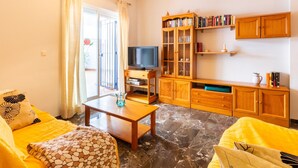 Uma sala de estar com sofá, mesa de centro, televisão, um aparador com livros e um lustre.