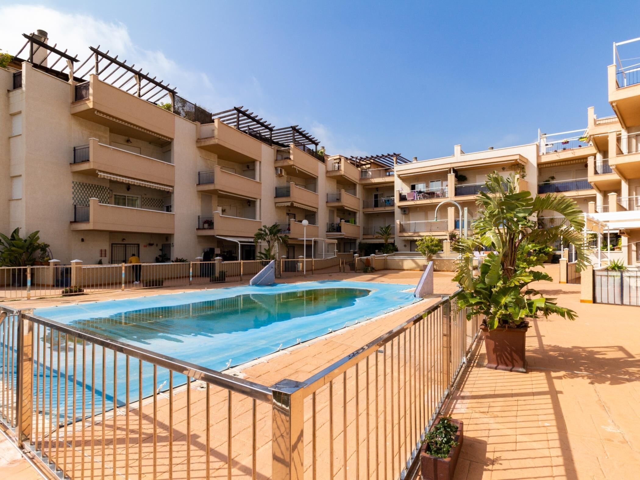 Un edificio residencial de varios pisos con piscina, balcones y plantas en macetas.