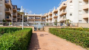 Um edifício residencial com várias andares, varandas, um caminho pavimentado e sebes bem cuidadas.