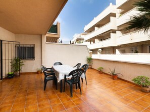 Une terrasse avec une table et des chaises, des plantes en pot et un sol carrelé.