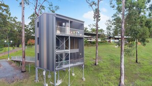 Un bâtiment moderne à plusieurs étages, doté d’un balcon au dernier étage, et entouré d’une zone verdoyante et d’arbres.