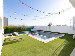 A modern outdoor pool area with a clear view of the mountains in the background, surrounded by well-maintained grass and a white wall.