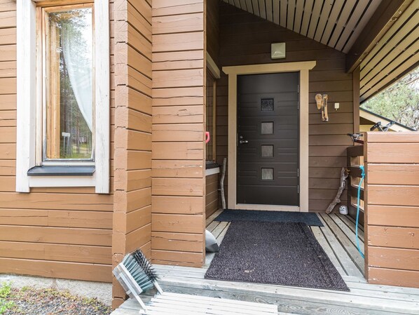 Una casa de fusta amb una porta fosca, una finestra amb cortina i un estri de porta.