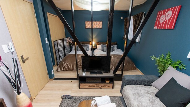 Un salon moderne avec un canapé, un téléviseur posé sur un meuble en bois, un lit avec une tête de lit et une plante décorative.