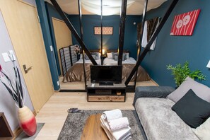 A modern living room with a sofa, a TV on a wooden stand, a bed with a headboard, and a decorative plant.