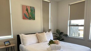 A neatly made bed with white linens and a bouquet of flowers, a cactus artwork on the wall, and a small bedside table with a picture frame. - Delicate Bundoora townhouse 10 (Bundoora)
