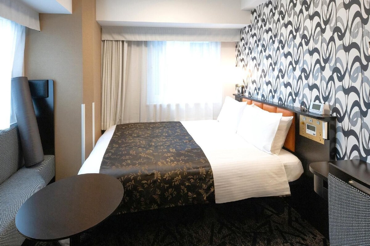 A hotel room with a bed, a desk, a chair, and a small table.