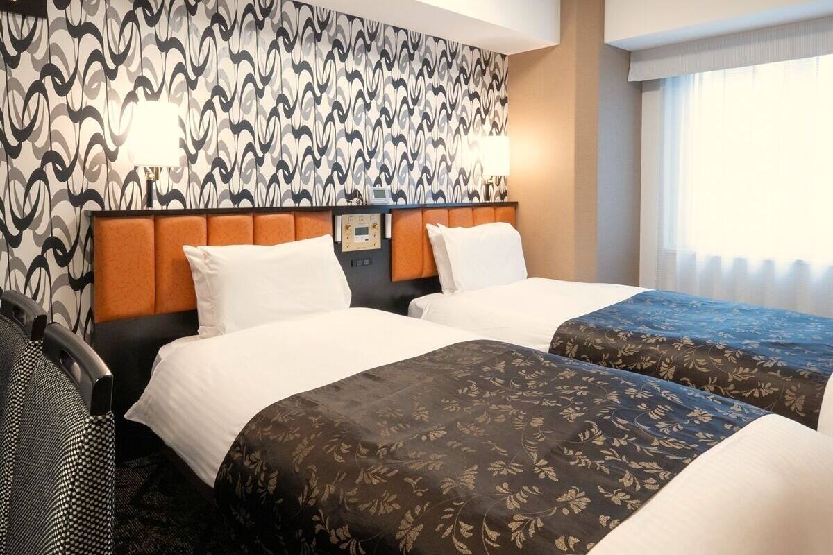 A hotel room with two beds, a patterned wall, a headboard, and a window with curtains.