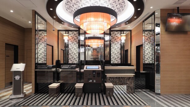 A modern hotel lobby with a central reception desk, patterned wallpaper, and a large chandelier. - APA HOTEL Nihombashi Bakuroyokoyama Ekimae (Tokyo)