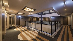 A modern hotel lobby with a central atrium, multiple elevators, and a patterned carpet. - APA HOTEL Nihombashi Bakuroyokoyama Ekimae (Tokyo)