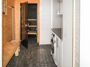 A compact kitchen with a washing machine, a bench, and a wooden door leading to a darker interior. - Kesäranta by Interhome (Enonkoski)