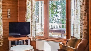 A cozy room with a television on a wooden stand, a small round table, a sofa, and a large window with curtains. - Kesäranta by Interhome (Enonkoski)
